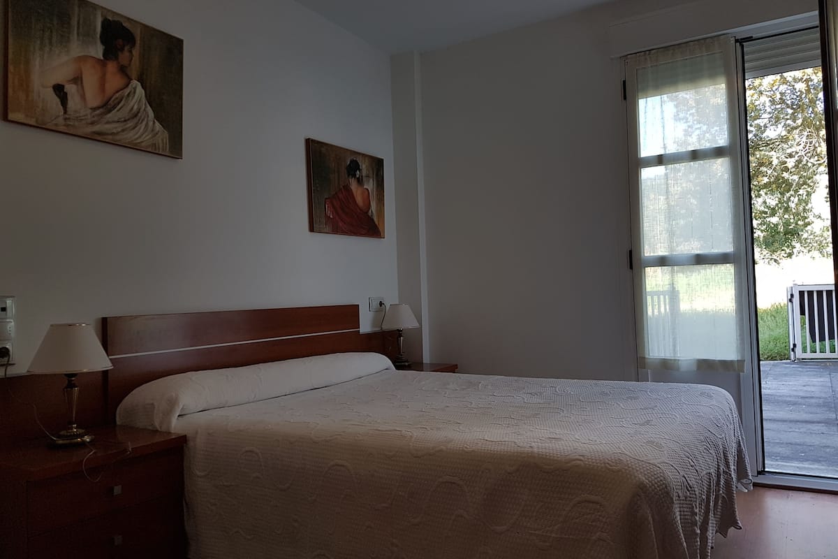 A bedroom with a large bed, a nightstand, a lamp, and two paintings on the wall.