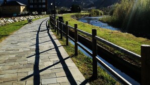 Un sendero pavimentado junto a un río, con una valla de madera y farolas.
