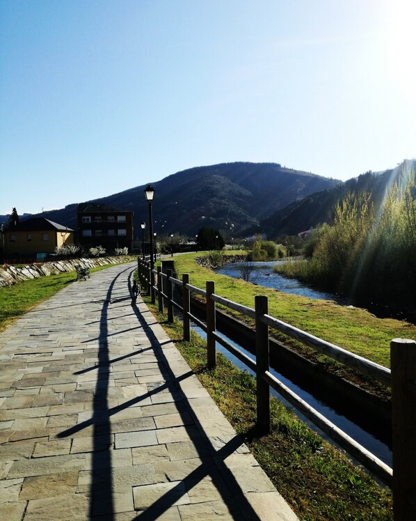 A paved pathway alongside a river, with a wooden fence and street lamps.