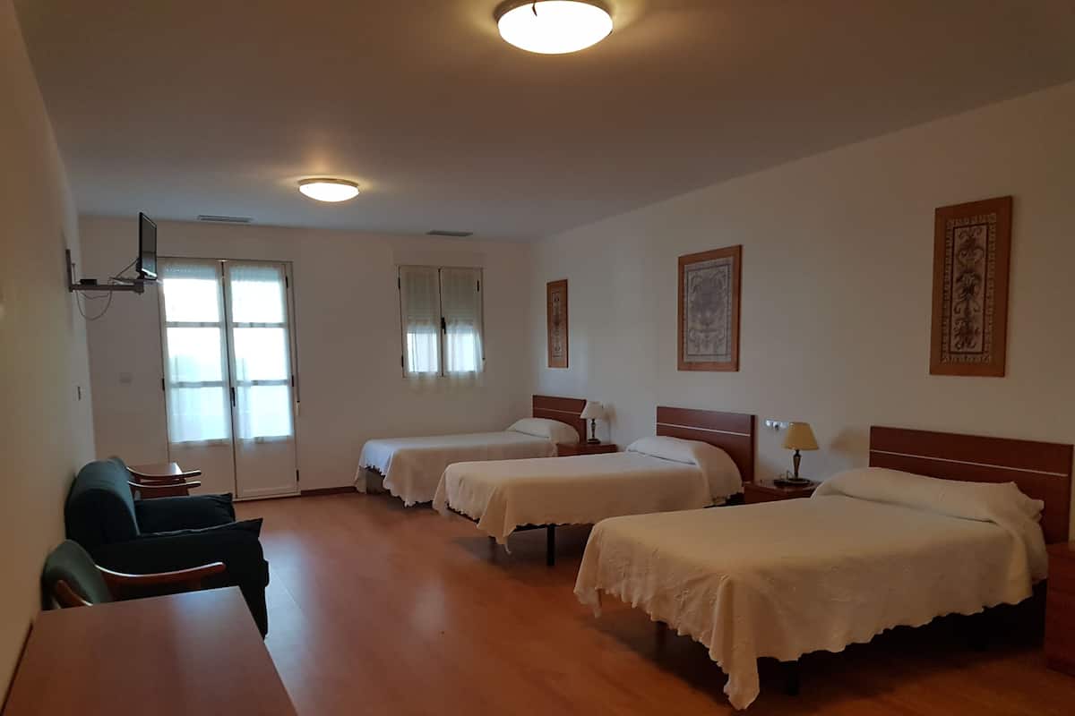 A hotel room with three beds, a desk, and a chair.