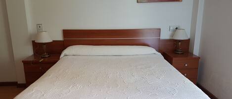 A neatly made bed with a white bedspread, wooden headboard, and two bedside lamps.