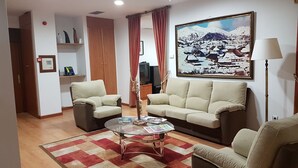Un salón con dos sofás, una mesa de centro de vidrio, un tapete rojo y beige, un cuadro de un paisaje nevado y una lámpara.