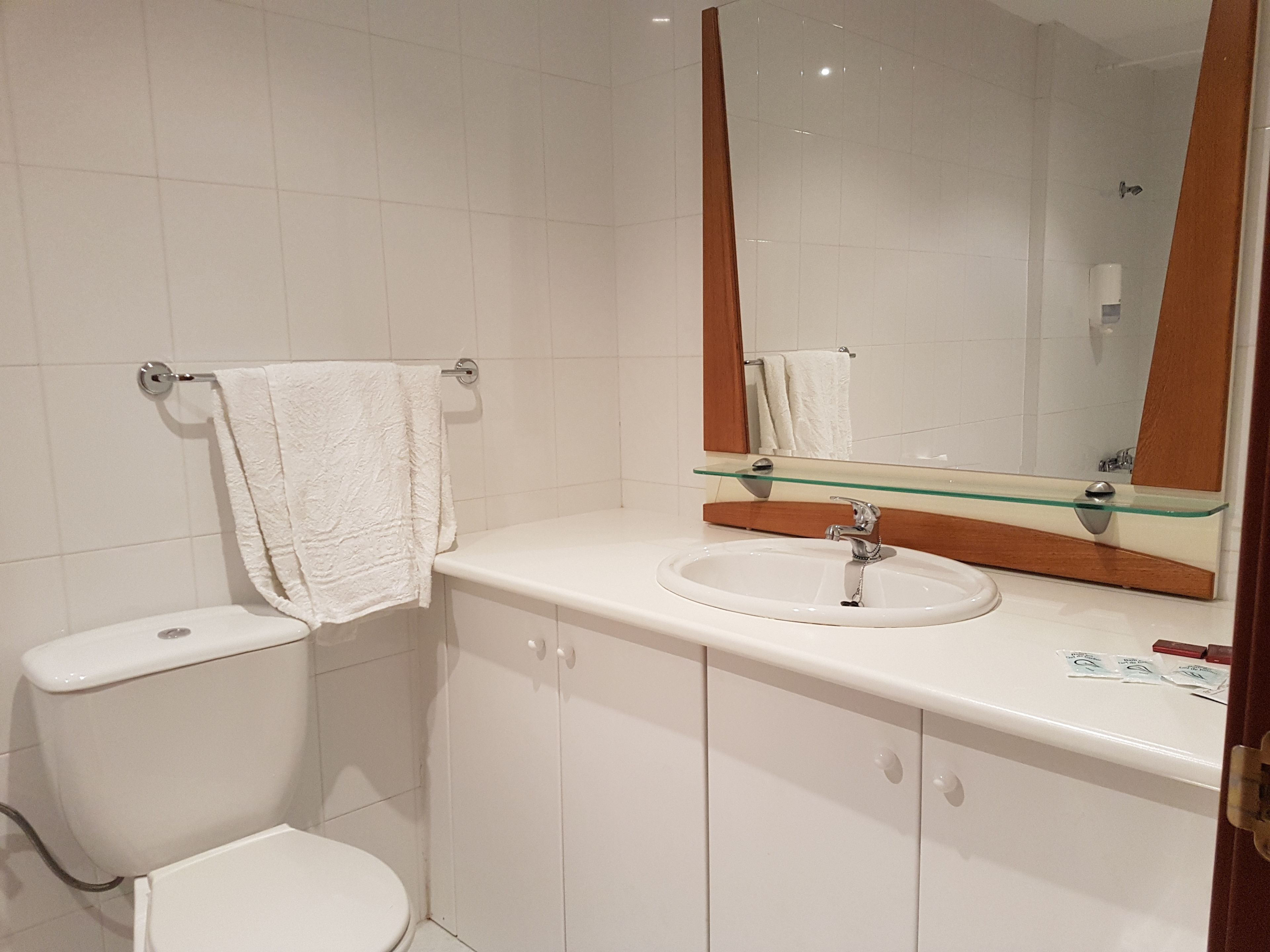 A bathroom with a white toilet, a glass-topped sink, and a mirror with a wooden frame.