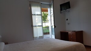 Un dormitorio con cama, cómoda, televisor montado en la pared y puerta corrediza de vidrio que da a un balcón.
