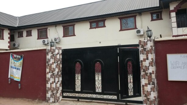A building with a gated entrance, multiple windows, and a signboard. - Kings Crown Hotel (Lagos)