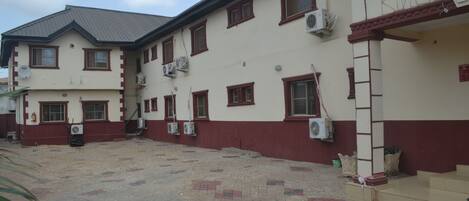 A two-story building with a tiled courtyard, multiple windows, and air conditioning units.