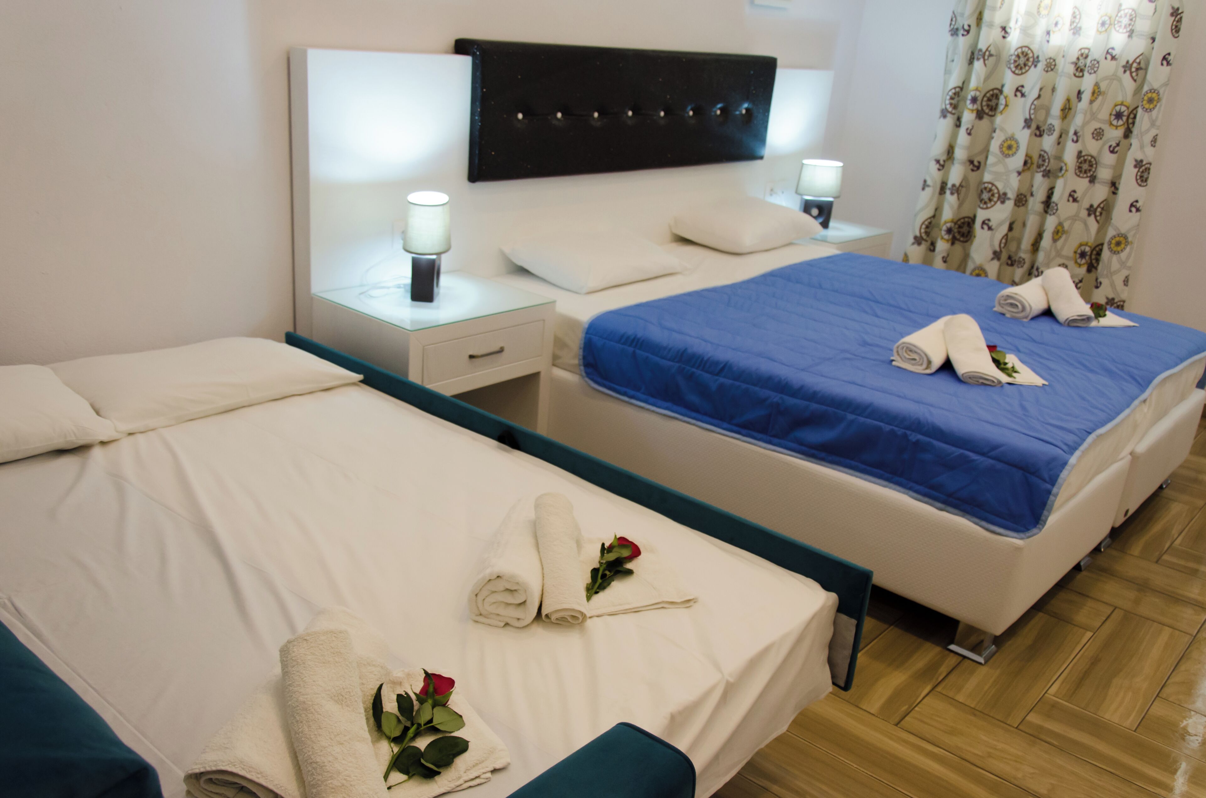 A hotel room with two beds, each with a different colored bedspread, a bedside table with a lamp, and a window with curtains.