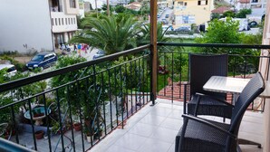 Un balcón con mesa y sillas, plantas en macetas y vista a una zona residencial con casas y coches.