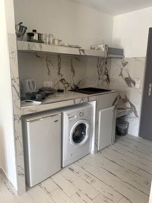 A compact kitchen with a built-in washing machine, a sink, and a stove. - Polykratis Rooms (Skiathos)