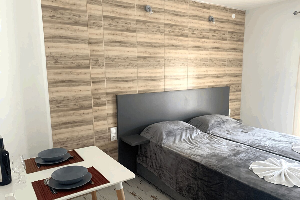 Un dormitorio moderno con una pared de madera, una cama con cabecera gris y una pequeña mesa con platos y cubiertos.