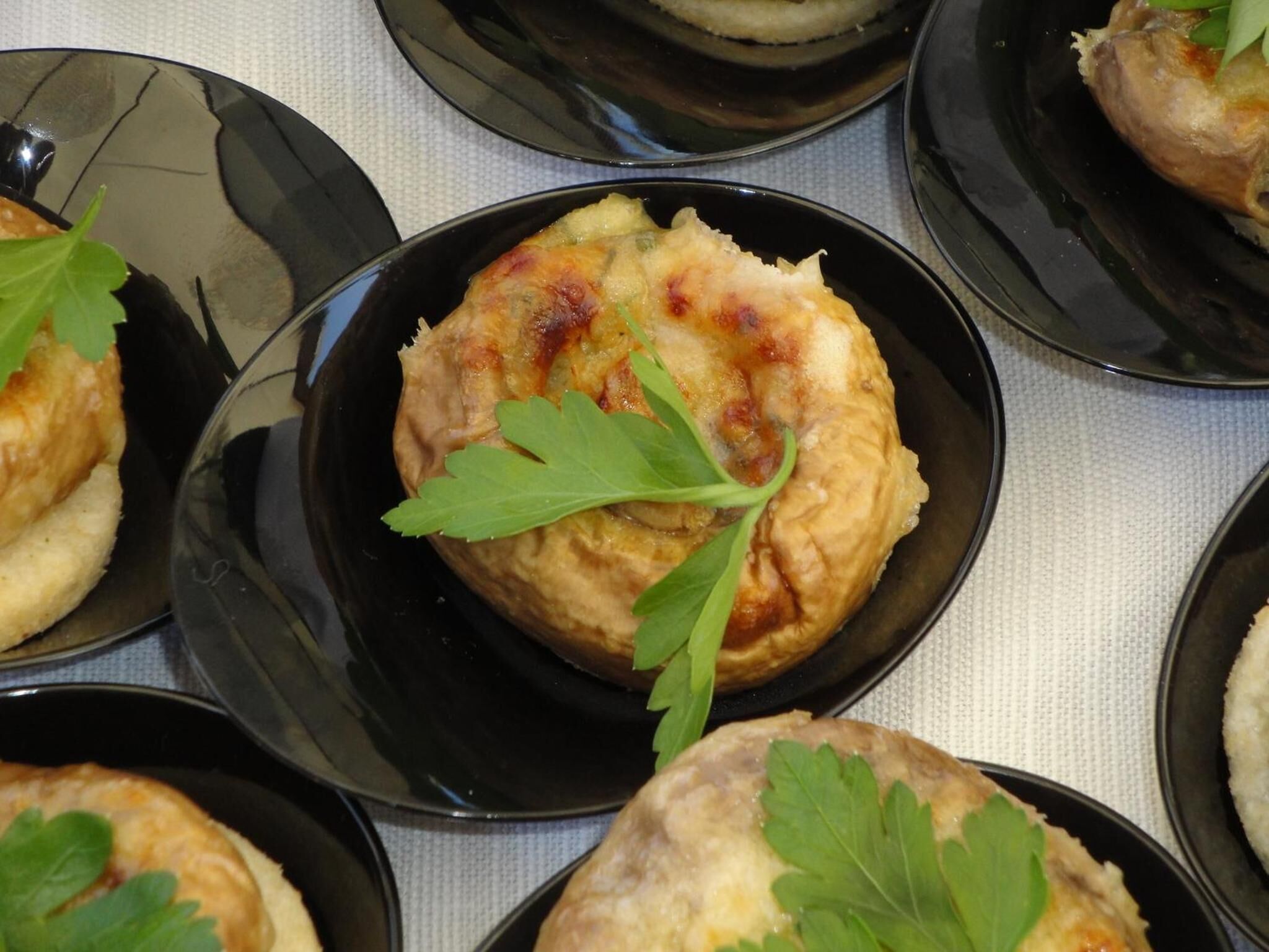 A series of black plates with food items, each garnished with a green leaf.