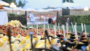 Ein gedecktes Open-Air-Buffet mit verschiedenen Speisen am Spieß, unter Zelten aufgebaut, mit einer Bühne im Hintergrund.