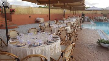 Een buitenterras met ronde tafels, rieten stoelen en parasols.
