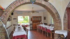 Ein Restaurant mit Ziegelbogen, Holztischen und Blick auf Grün.