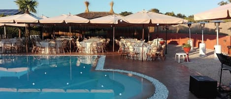 A pool area with tables and chairs, surrounded by umbrellas and solar heaters.