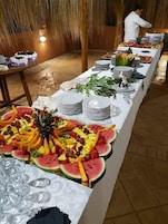 A buffet table with various fruits and a chef preparing food in the background.
