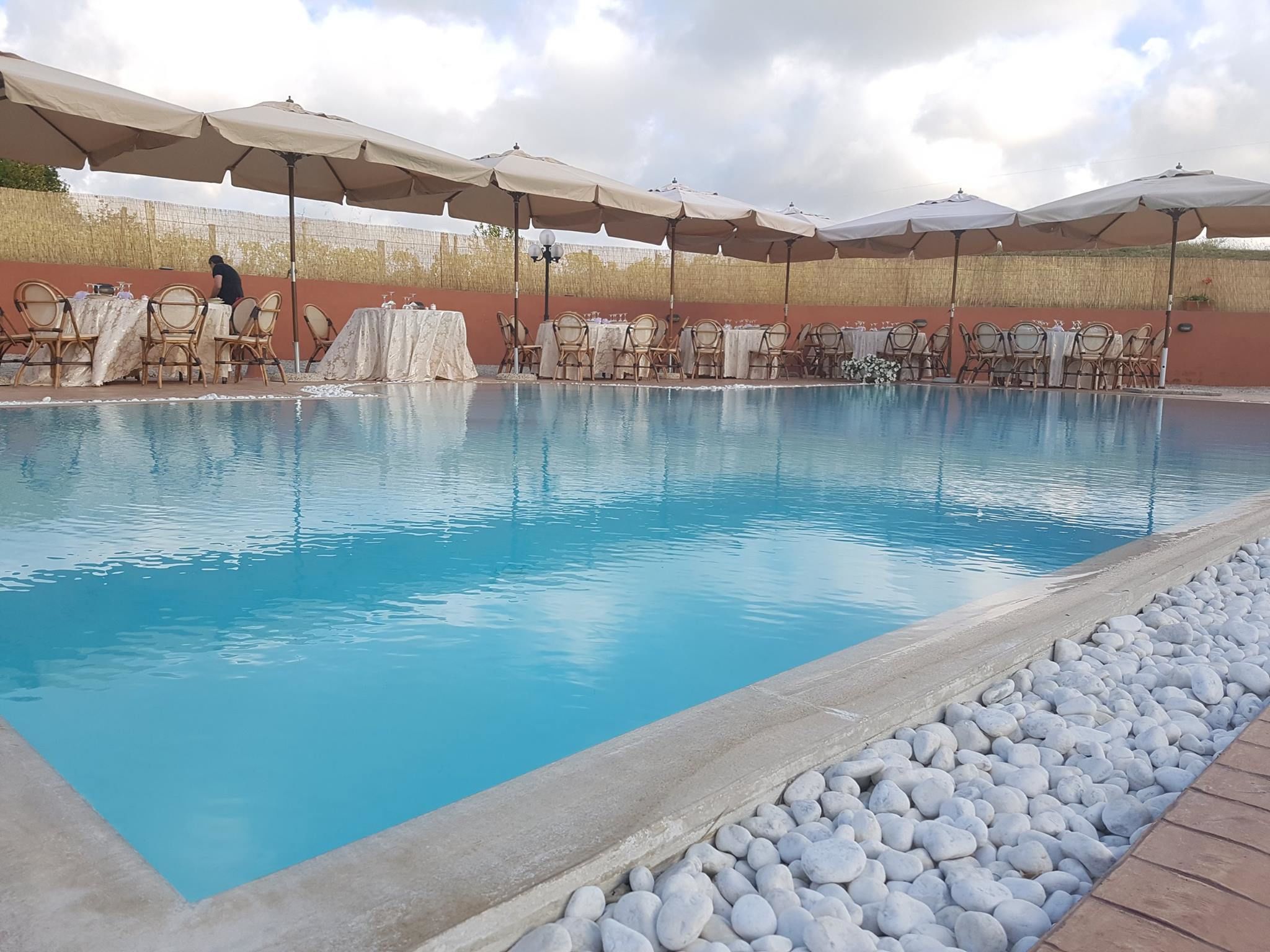 Ein Swimmingpool mit Liegestühlen und Sonnenschirmen, umgeben von einer Steinmauer.