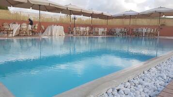 Ein Swimmingpool mit Liegestühlen und Sonnenschirmen, umgeben von einer Steinmauer.