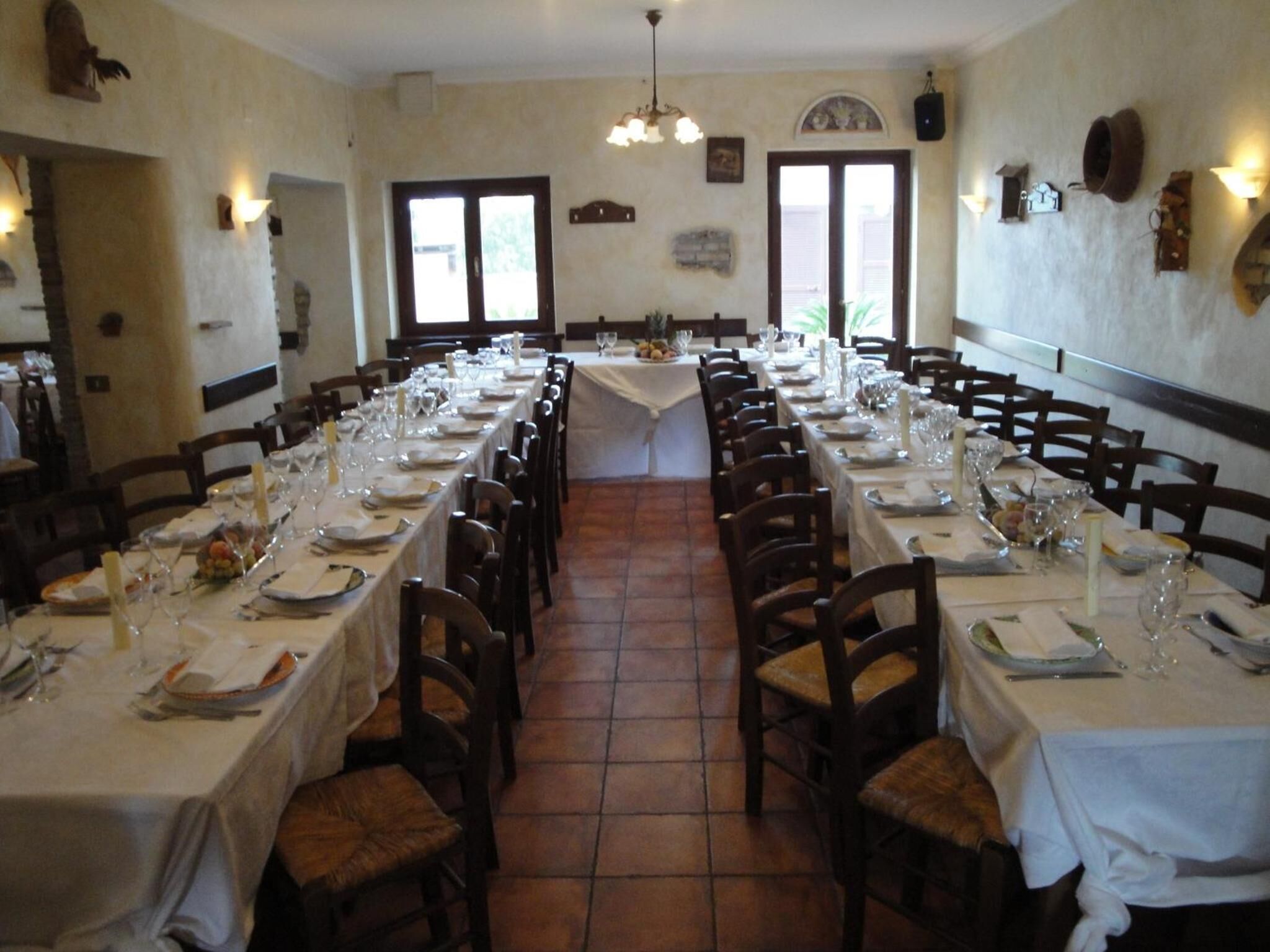 Une longue table à manger, dressée pour un repas, avec des chaises de chaque côté, un sol carrelé et un lustre.
