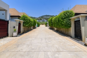 A residential street with houses on either side, a clear sky, and a hilly landscape in the background. - Thai Villa Rawai (Rawai)