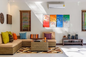 A living room with a sectional sofa, a coffee table, and a TV stand with speakers. - Thai Villa Rawai (Rawai)