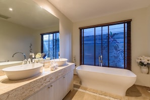 A modern bathroom with a freestanding bathtub, two sinks, and a large mirror.
