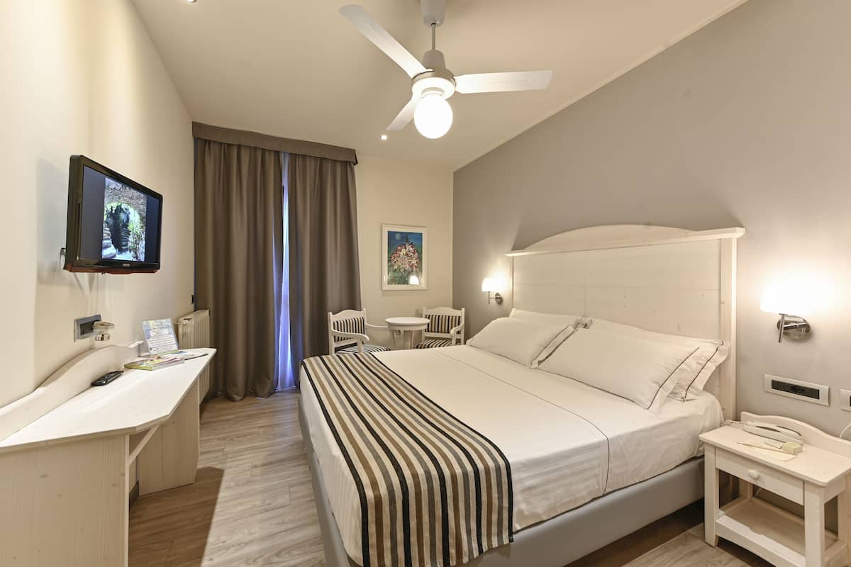 A hotel room with a bed, bedside table, desk, and a television on the wall.