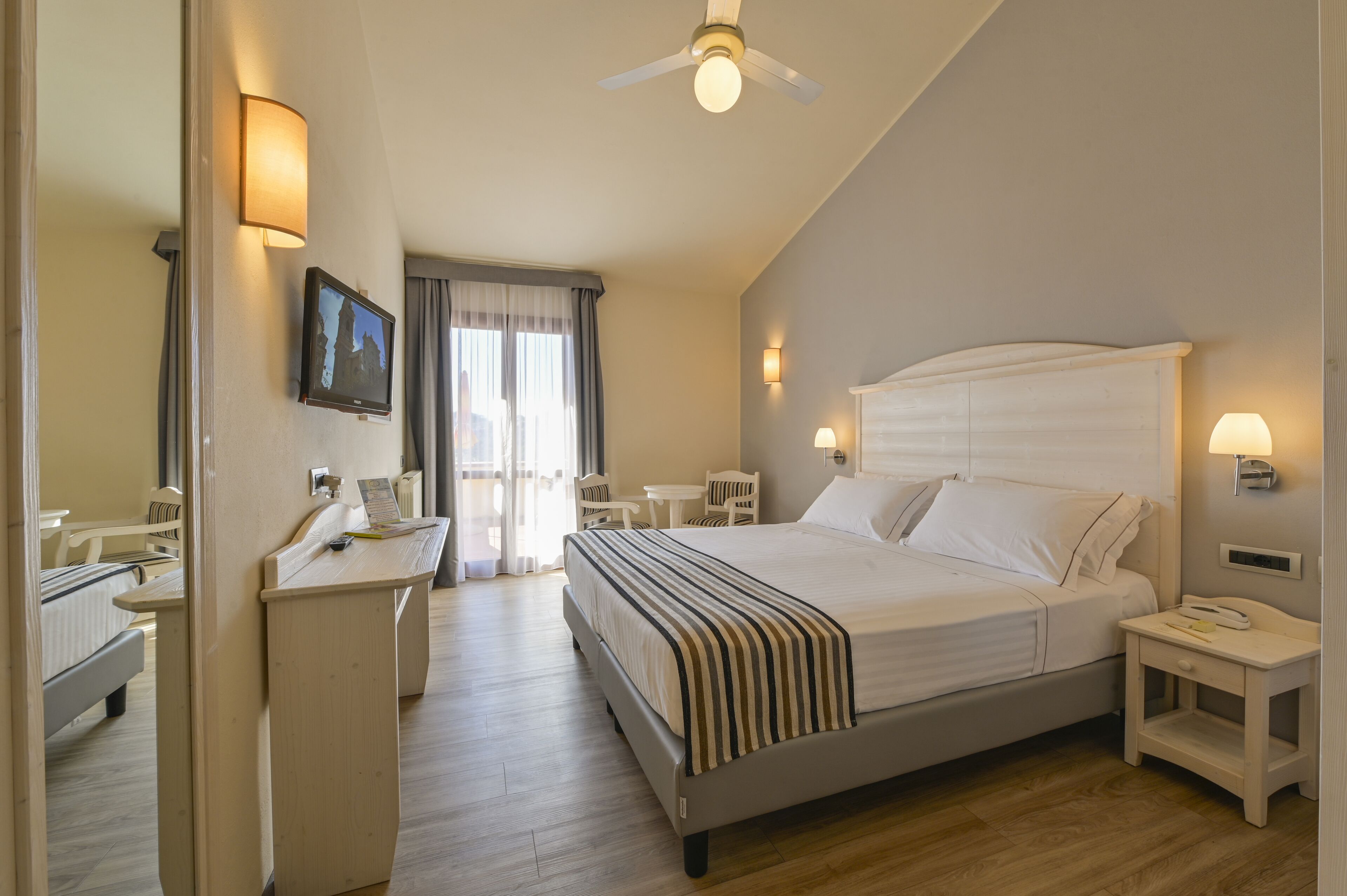 Habitación de hotel con cama, mesita de noche, escritorio, silla y televisor en la pared.