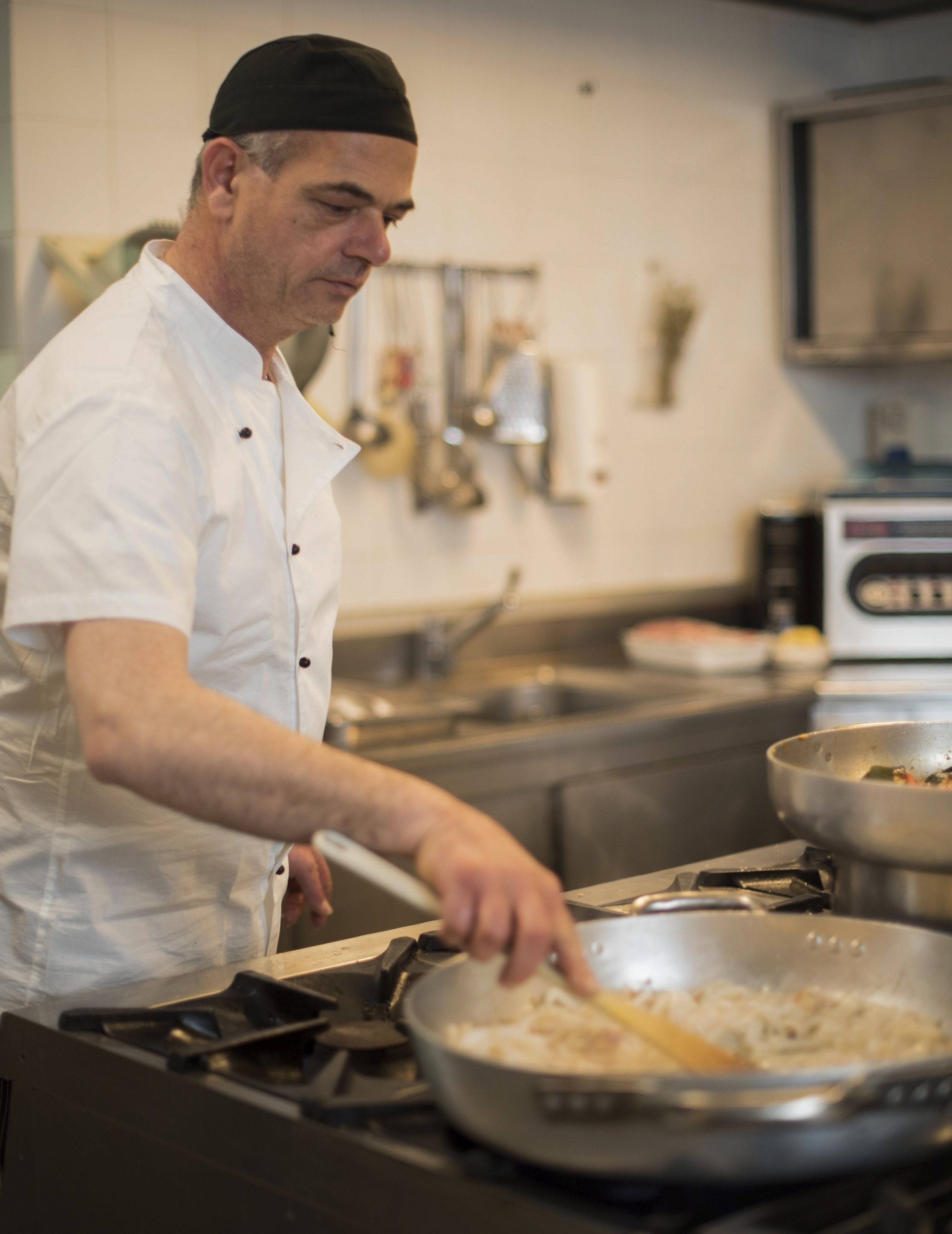 Un chef con uniforme blanco cocina en una cocina con electrodomésticos de acero inoxidable y salpicadero de azulejos.