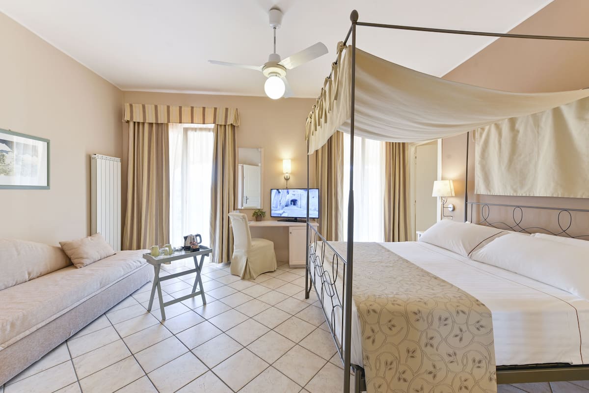 A hotel room with a four-poster bed, a desk with a chair, a television, and a sofa.