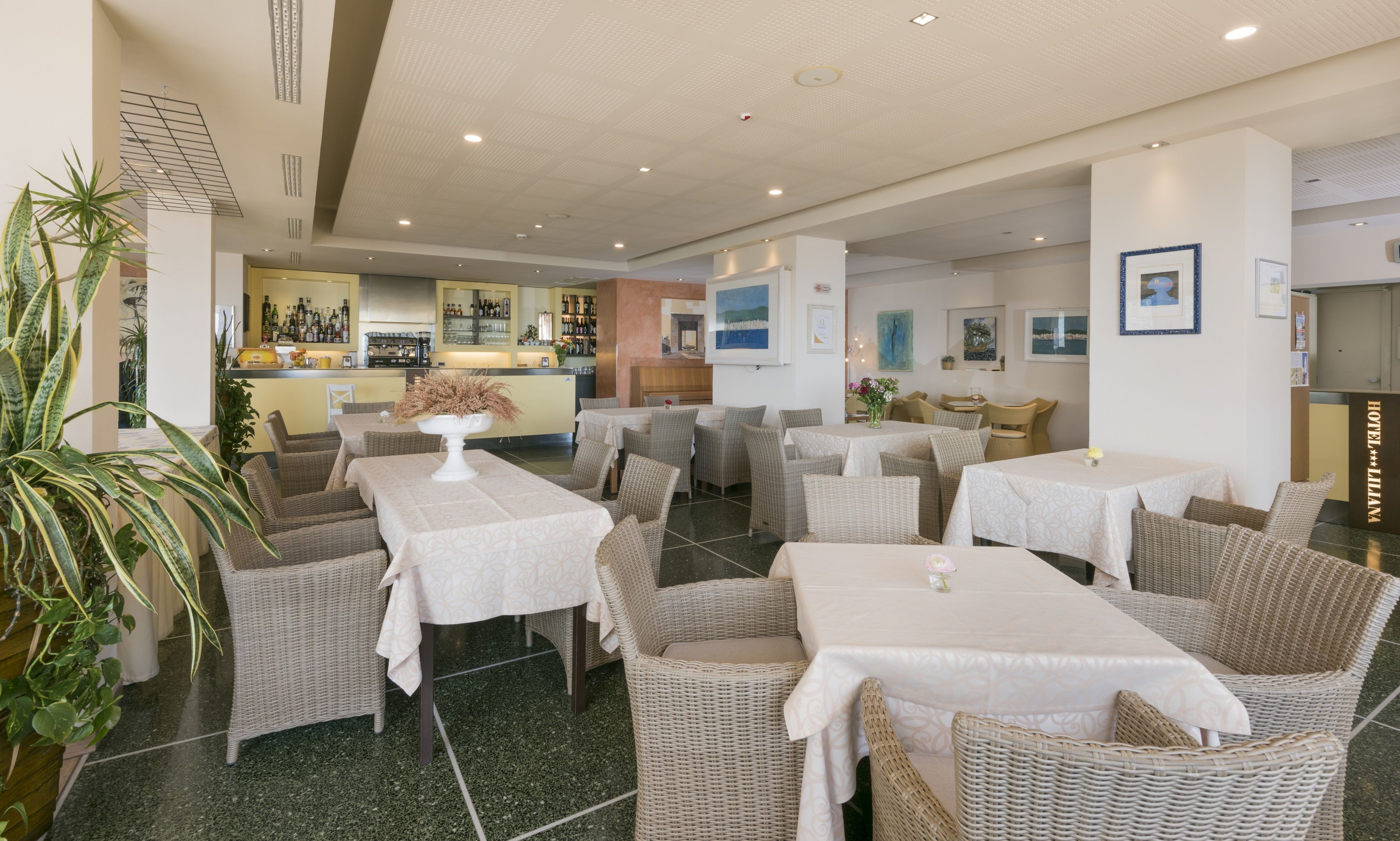 Una hall d'albergo con arredi in vimini, un'area bar e opere d'arte alle pareti.