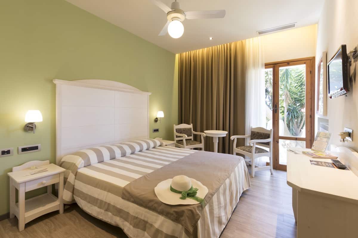 A hotel room with a large bed, a desk, a chair, a small table, a TV, and a window with curtains.