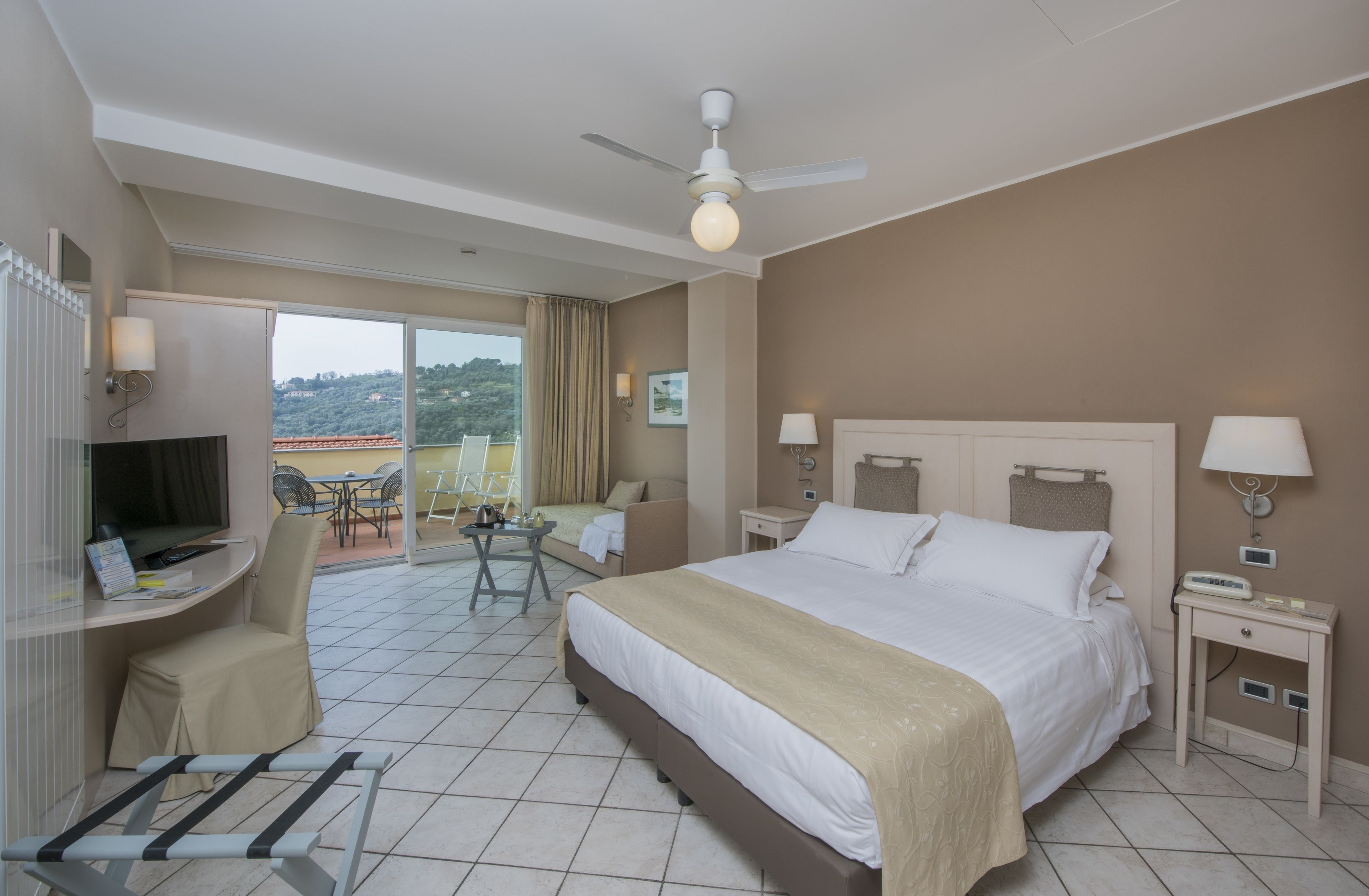 Habitación de hotel con cama, escritorio, silla y balcón con vistas.