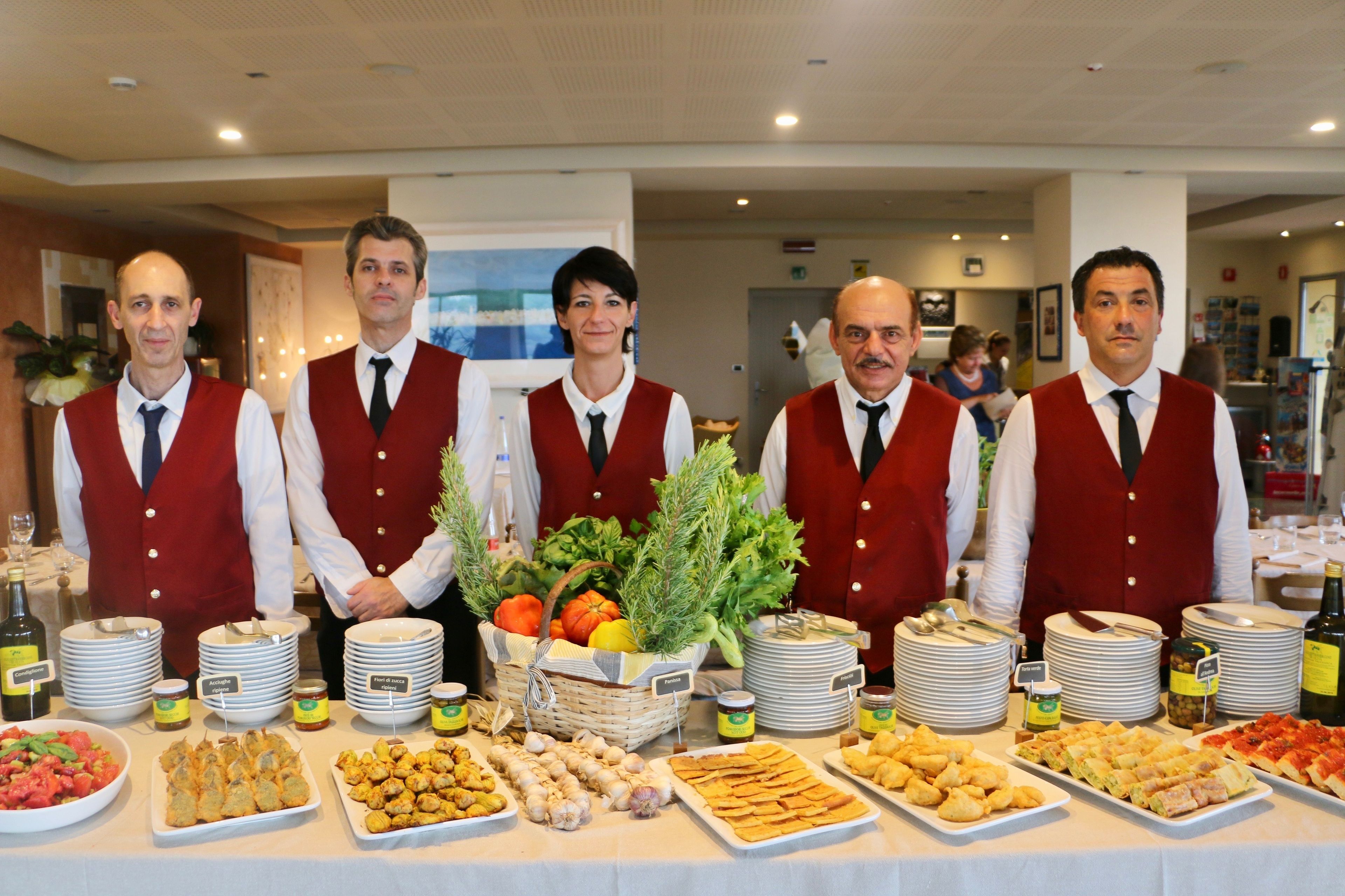 Une table de buffet garnie de divers plats et un groupe de serveurs portant des gilets rouges.