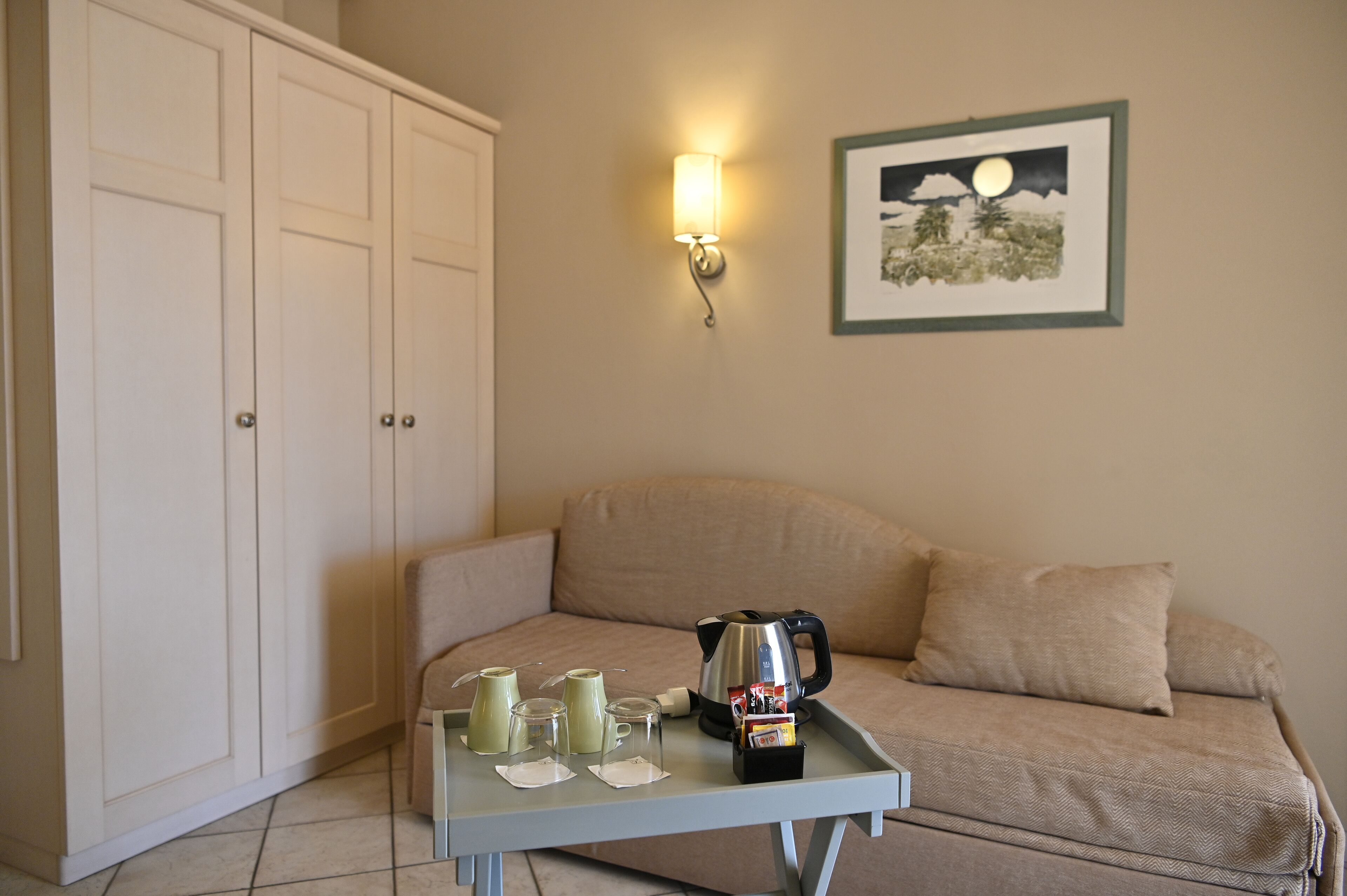 A room with a beige sofa, a coffee table with a kettle and cups, and a framed picture on the wall.