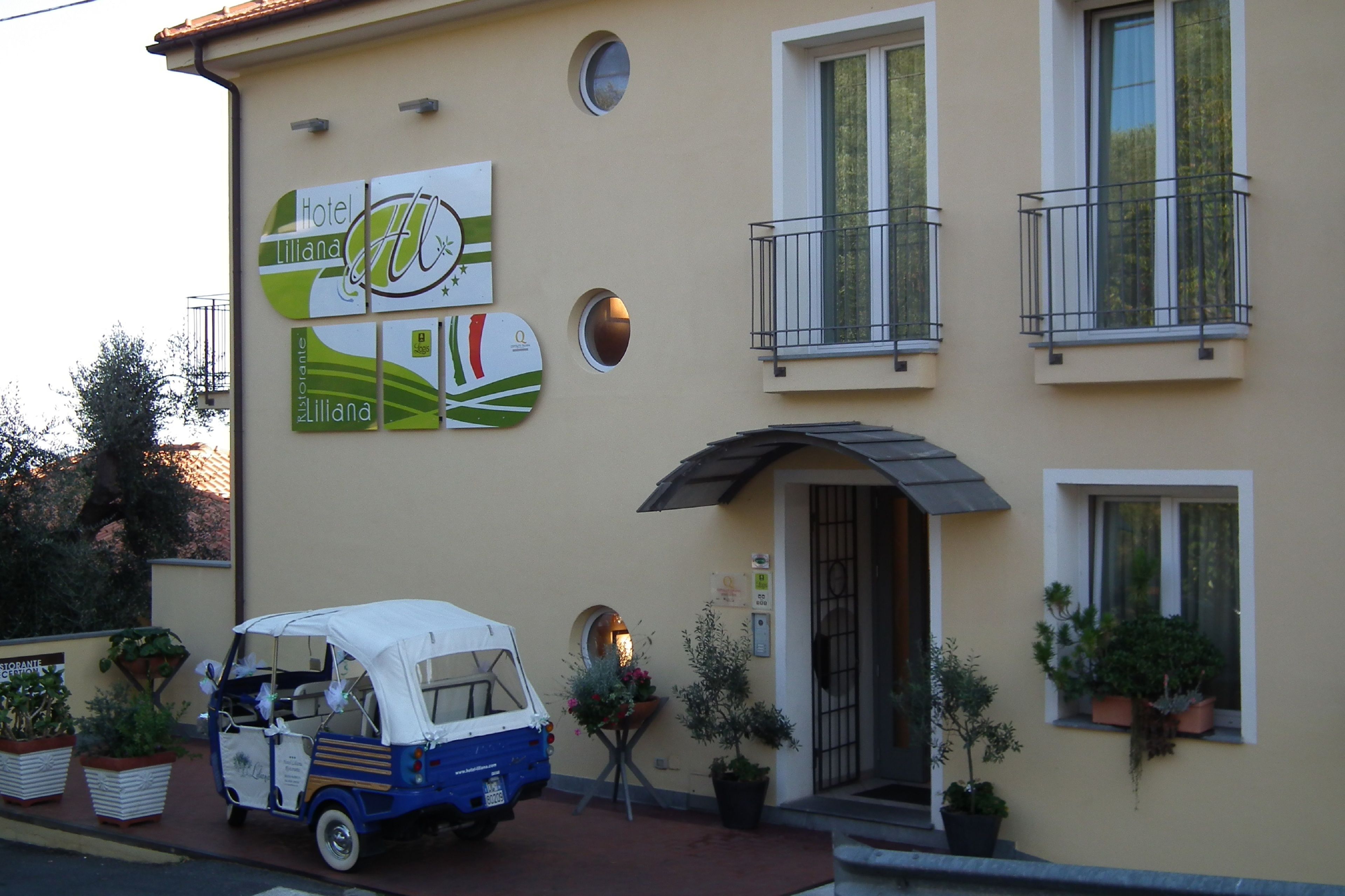 Un edifici amb un cartell de l'Hotel Liliana, un vehicle petit blau i blanc estacionat a la façana, i plantes en testos a la vorera.
