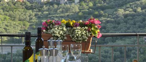 Una mesa dispuesta para comer, con botellas y copas de vino, un arreglo floral y una vista panorámica de un pueblo en la ladera.