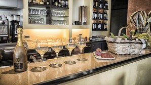 A bar area with a bottle of Valdo wine, three glasses of white wine, a basket of snacks, and shelves of wine bottles and glasses in the background. - Hotel Liliana Diano Marina (Diano Marina)