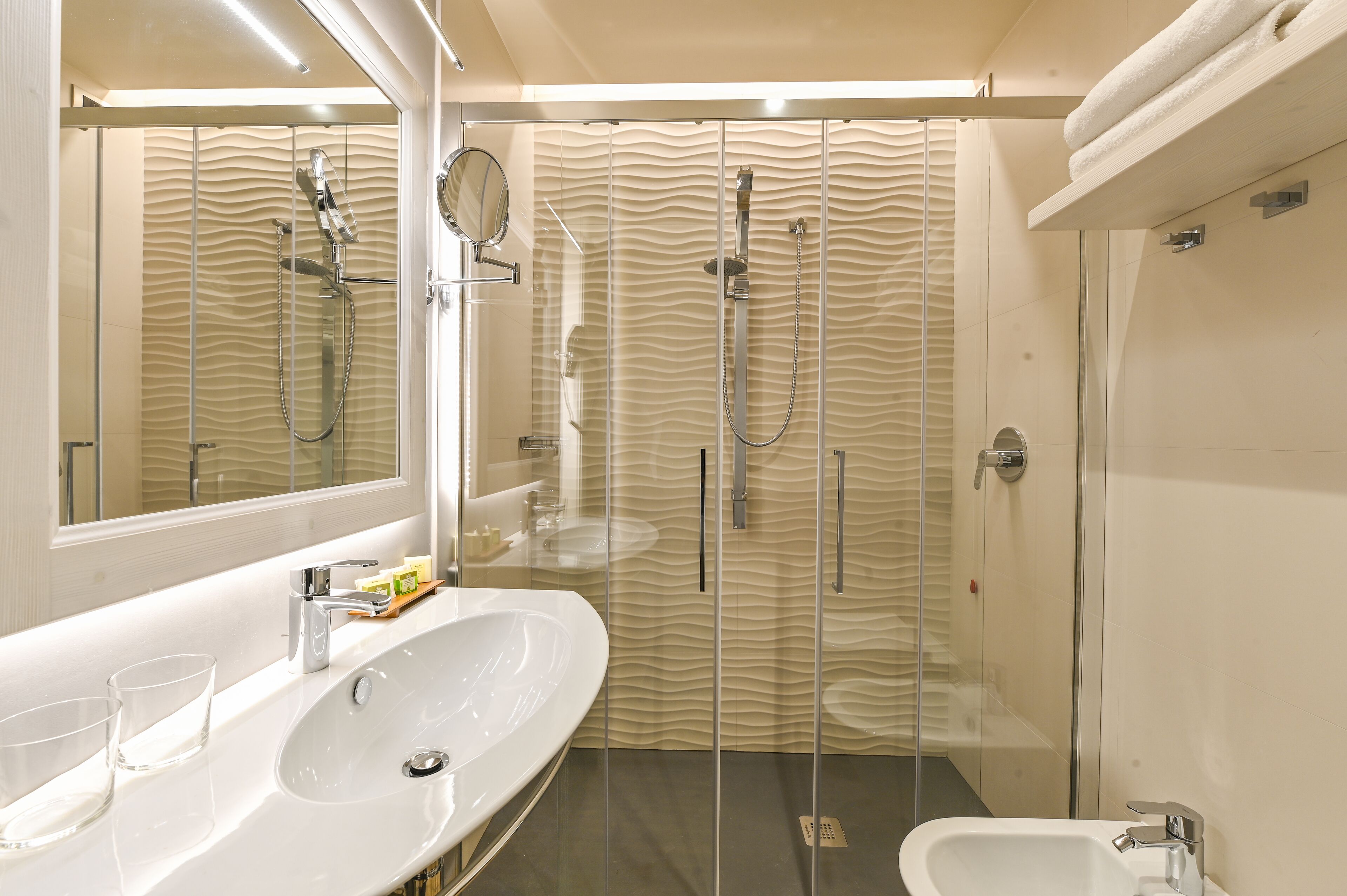 A modern bathroom with a glass-enclosed shower, a large white sink, and a mirror.