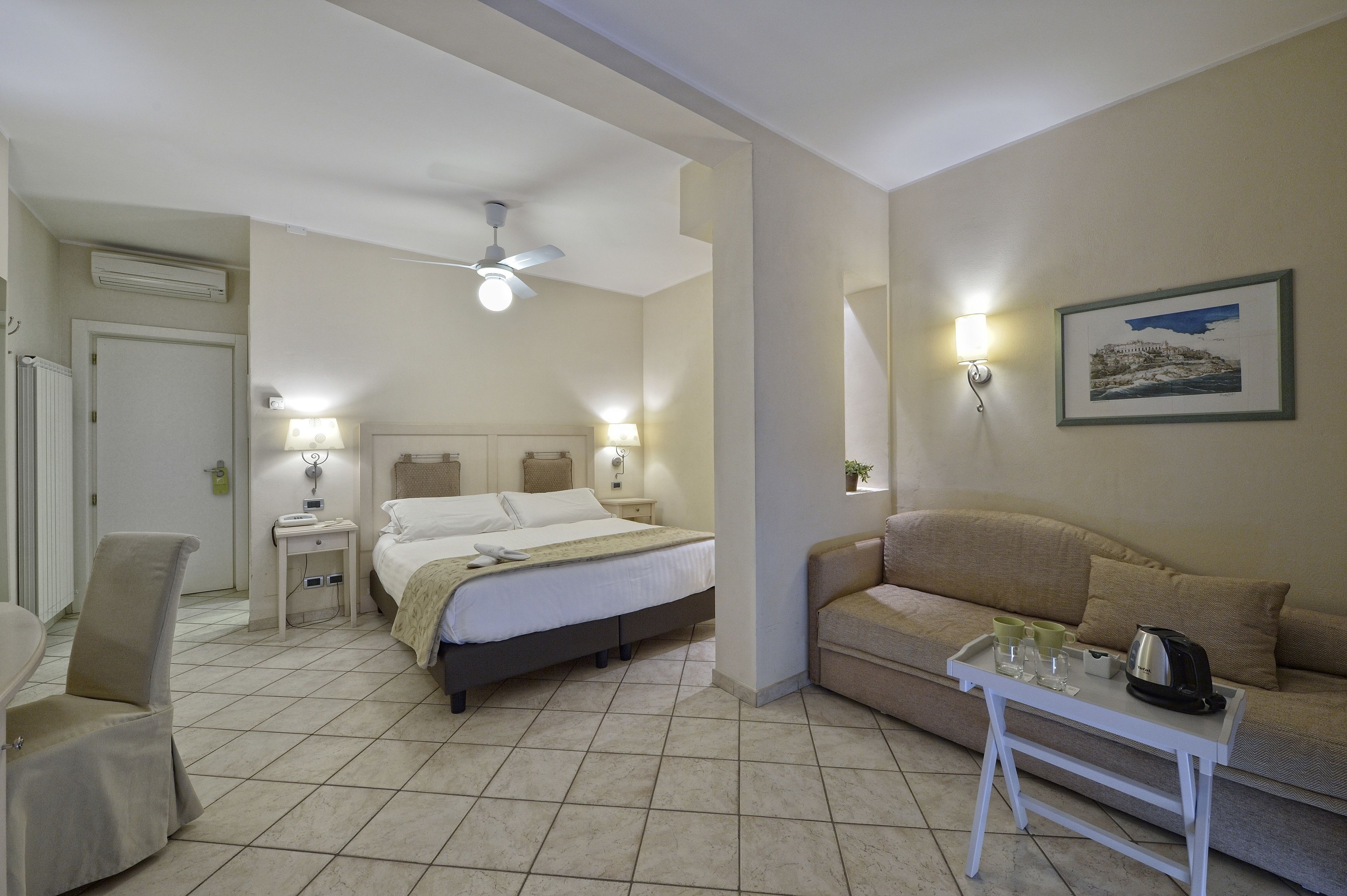 A hotel room with a bed, bedside tables, a sofa, a small table with a tray, and a ceiling fan.