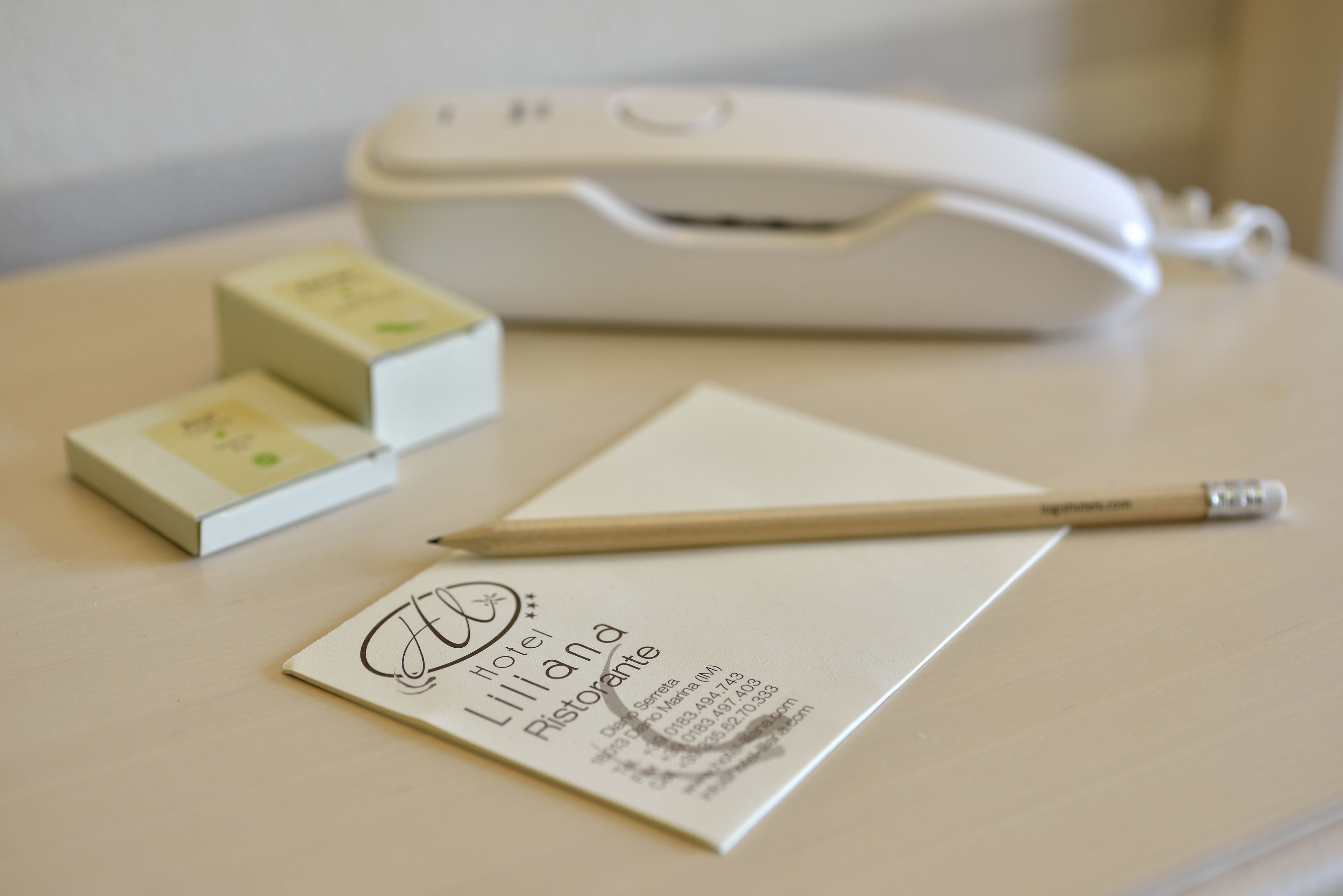 A business card for Hotel Liliana Restaurante on a wooden table with a white printer and two small boxes.