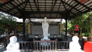 A covered pavilion with a statue in the center, surrounded by potted plants and a railing.