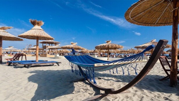 Una playa con hamacas, sillas de sol y sombrillas de paja.