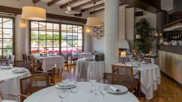 Un restaurante con mesas redondas, manteles blancos y sillas de mimbre.