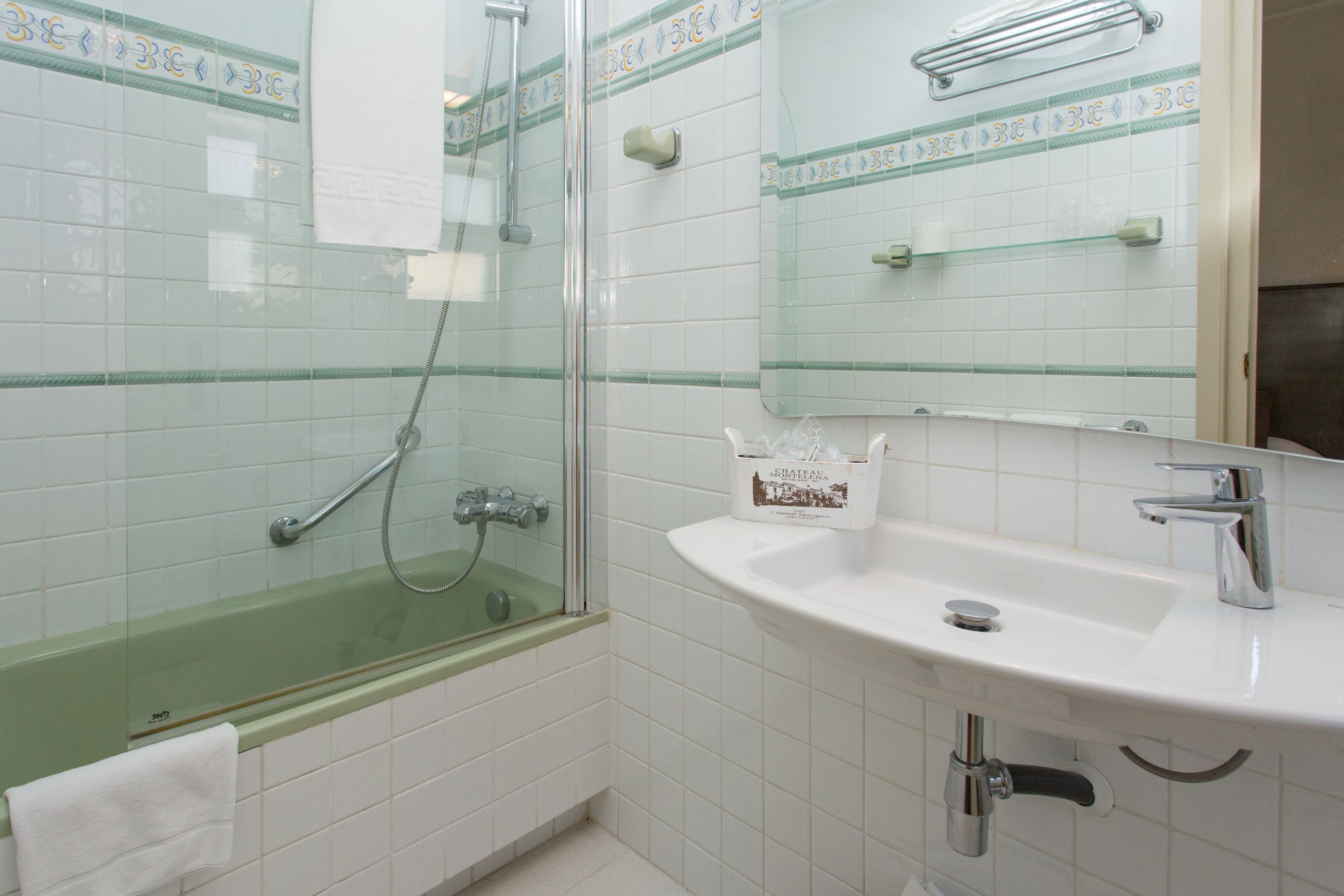 Un baño con ducha envuelta en vidrio, un lavamanos blanco y un espejo encima.
