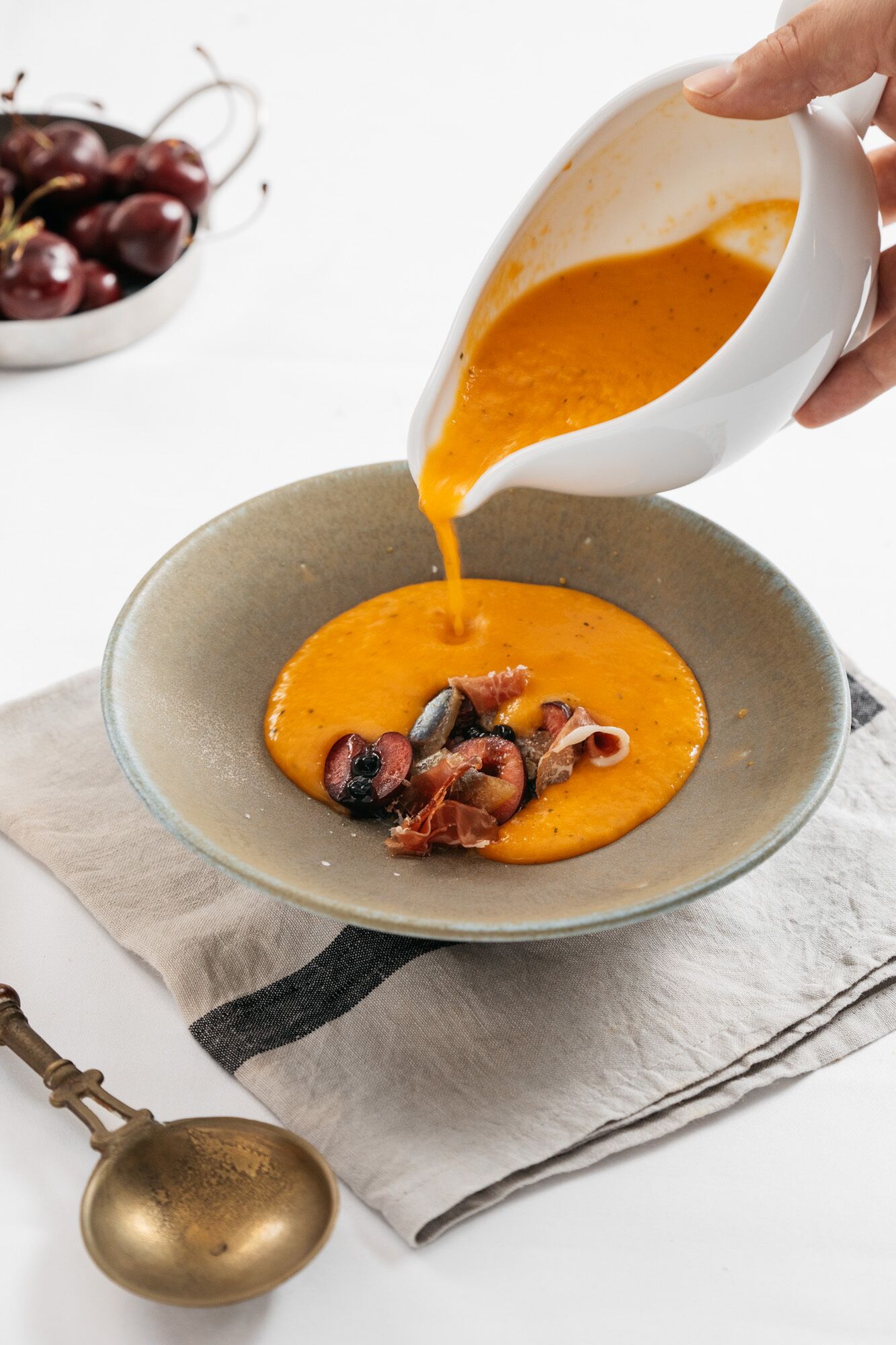 Un tazón de sopa de naranja siendo servido sobre un plato con diversos ingredientes.
