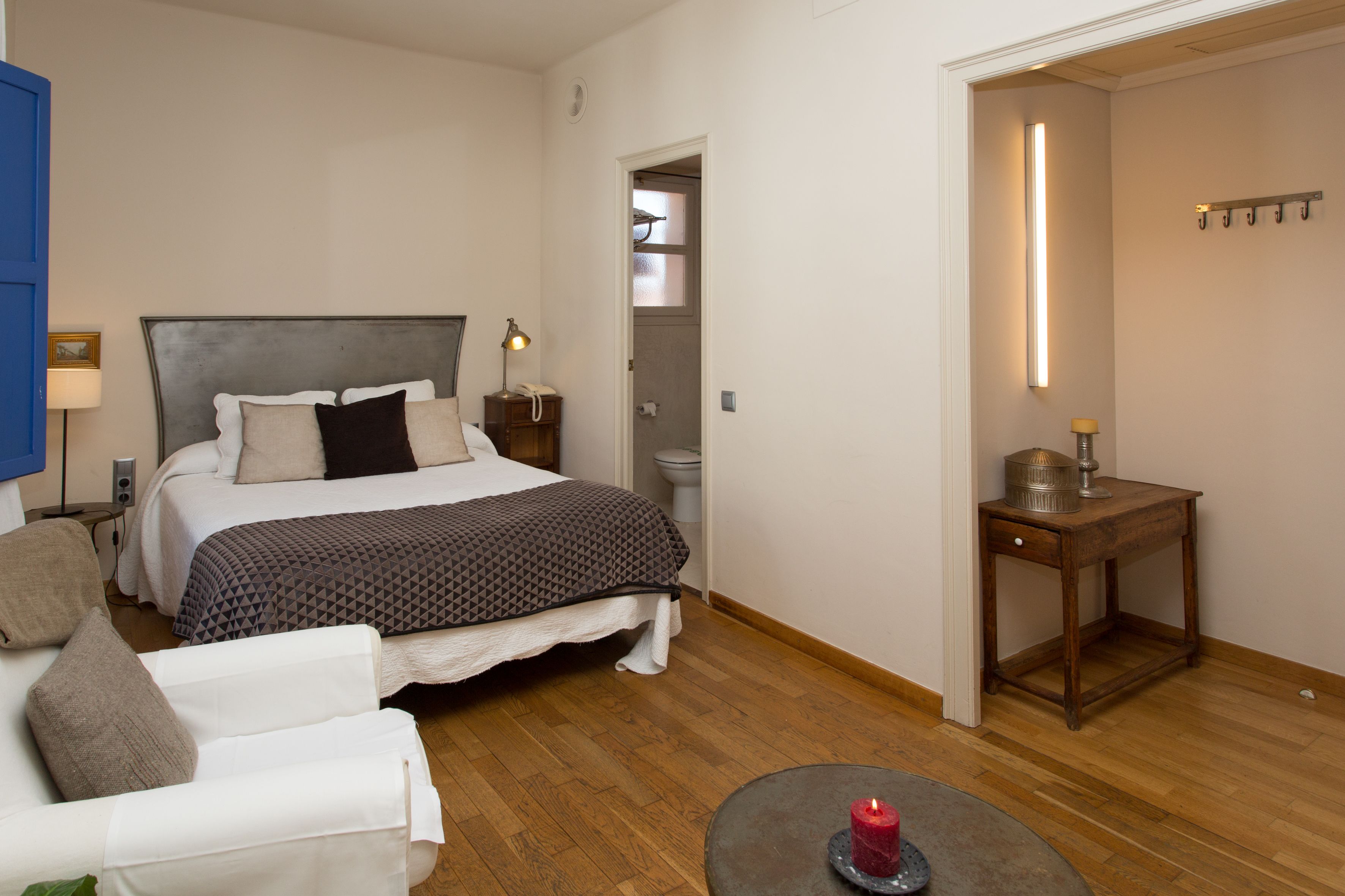 Un dormitorio con cama, mesita de noche, lámpara y una pequeña mesa con una vela.