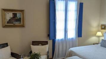 A hotel room with a bed, a chair, a small table with a plant, a lamp, and a framed picture on the wall.