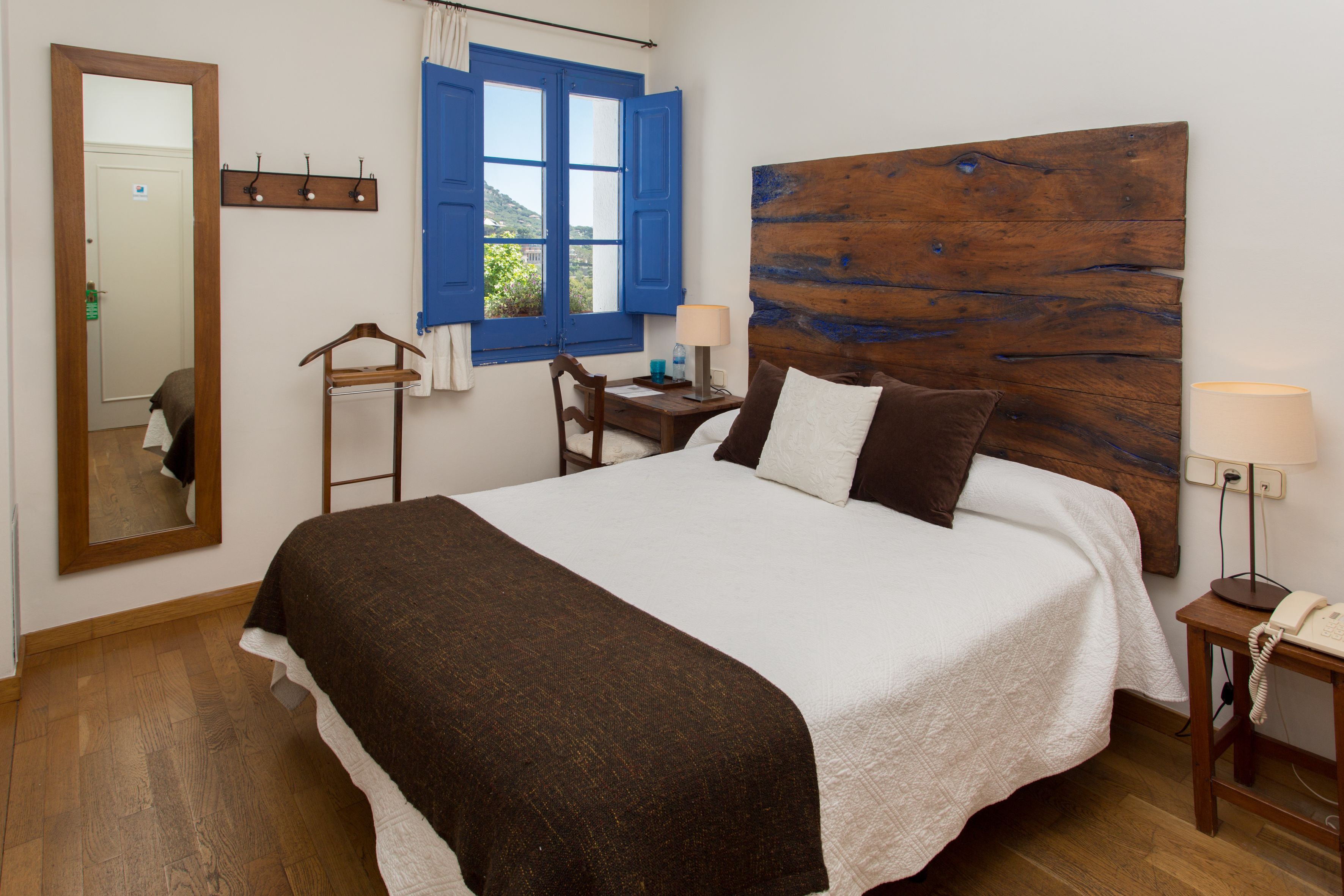 A neatly made bed with a wooden headboard, a bedside table with a lamp, a chair, and a mirror on the wall.