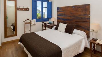 A neatly made bed with a wooden headboard, a bedside table with a lamp, a chair, and a mirror on the wall.